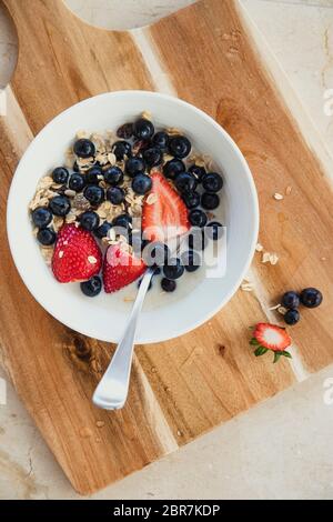 Portrait d'un nouveau petit-déjeuner sain. Il y a des fruits, de l'avoine et le lait dans un bol avec une cuillère. Le bol est placé sur une planche à découper en bois boar Banque D'Images