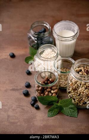 Granola de grain de millet croustillant maison avec fruits secs et noix, yaourt, lait, muesli dans différents pots de verre, menthe. Fond marron. Santé Banque D'Images