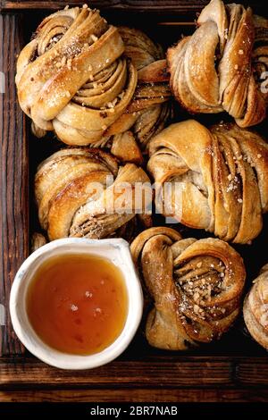 Gros plan des pains sucrées de cardamome suédois traditionnels Kanelbulle dans un plateau en bois et un bol de sirop. Pose à plat Banque D'Images