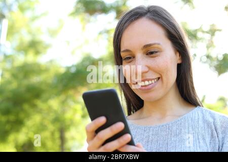 Happy woman standing outdoors message smart phone dans un parc Banque D'Images