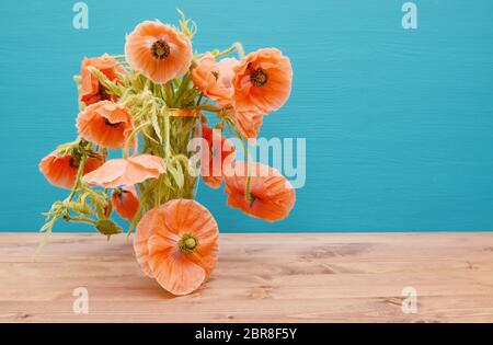 De nombreuses et belles roses coupées avec de longues tiges sinueuses coquelicots, débordement d'un vase en verre sur une table en bois, contre un fond bleu turquoise peint Banque D'Images