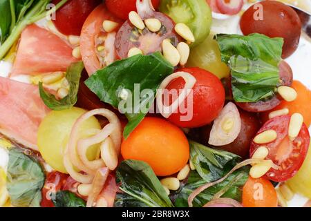 Détail d'une salade de tomates fraîches colorées avec des tranches d'échalotes, les noix de pin et de feuilles de basilic Banque D'Images