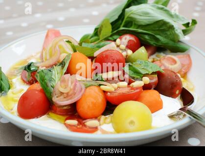 Salade de tomates mélangé avec des tomates cerises, noix de pin et les feuilles de basilic, habillé avec le mascarpone et huile d'olive Banque D'Images