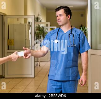 L'âge moyen, de race blanche, blanc male doctor in scrubs avec stéthoscope acceptant la carte blanche, troubles de couloir de l'hôpital en arrière-plan Banque D'Images