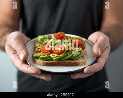 Prend les mains avec plaque sandwich vegan. Appetiezer sain - toast de pain de blé entier avec de l'avocat, les tomates cerises et les olives Banque D'Images