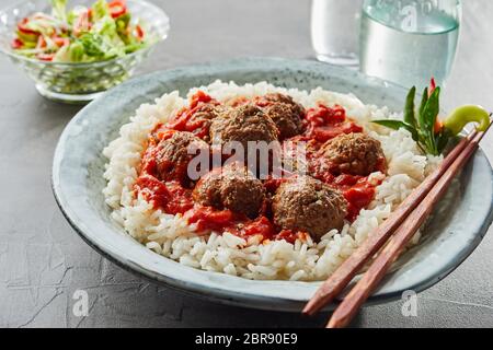 Riz frit délicieux avec des boulettes de viande et la sauce dans un bol blanc près de verre d'eau et un petit bol holding vegetables Banque D'Images