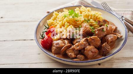 Spiral plat de pâtes fusilli avec dés de porc et les tomates dans un bol à côté de fourchette et couteau sur table en bois Banque D'Images