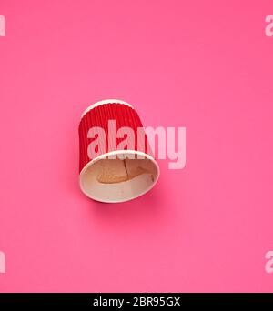 Tasse rouge en papier avec les bords ondulés par le café à l'envers sur un fond rose Banque D'Images