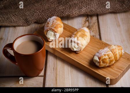 Rouleaux de pâte feuilletée avec de la crème sur un support en bois dans un style rustique Banque D'Images