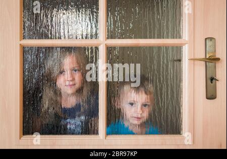 Portrait of a cute little Young boy and girl se cacher derrière une porte avec des fenêtres en verre tout en jouant à cache-cache Banque D'Images