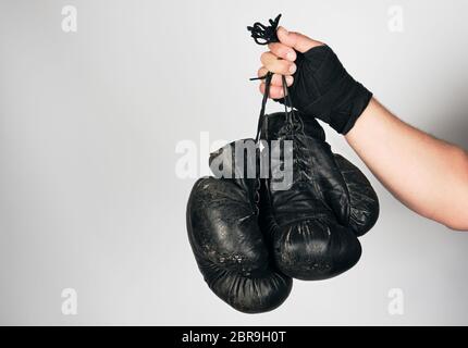 Le bras de l'homme enveloppé dans un bandage élastique noir sports détient old vintage paire gants de boxe en cuir, fond gris, copy space Banque D'Images