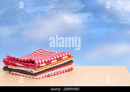 Pile de serviettes. Pile de serviettes de cuisine coton coloré plié sur une table lumineuse contre abstract blue ciel nuageux. Modèle pour votre produit d'affichage m Banque D'Images