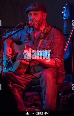 Chanteur de folk masculin, assis comme il chante et joue de la guitare, en concert intérieur. Banque D'Images