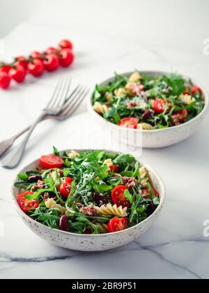 Salade chaude avec thon, arugula, tomates, haricots rouges, pâtes.idée et recette pour un déjeuner ou un dîner sain.deux bols avec salades chaudes sur table en marbre. Idées Banque D'Images