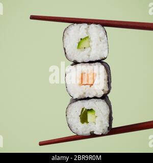 Trois rouleaux de sushi maki à l'algue nori, riz, saumon et d'avocat de l'affiche avec des baguettes sur un carré fond vert Banque D'Images