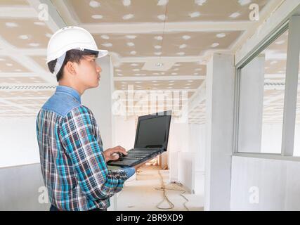 Faites l'inspection de la construction intérieure avec un ordinateur portable et portez un casque de sécurité en plastique blanc Banque D'Images