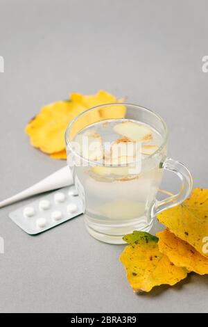Nourriture et boissons, encore concept de soins de santé de la vie. Boisson à infusion de thé au gingembre dans une tasse de verre, feuilles jaunes, thermomètre, pilules sur table, grippe froide hiver Banque D'Images