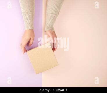 Fille tenir une boîte carrée brun violet sur un fond beige, vue du dessus, concept de donner des cadeaux Banque D'Images