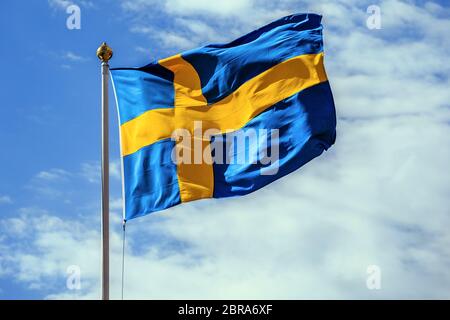 Le drapeau national de la Suède sur fond de ciel bleu avec des nuages. Banque D'Images