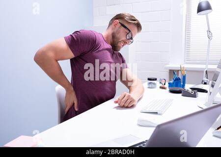 Vue latérale d'un jeune homme assis sur une chaise de bureau à avoir mal au dos Banque D'Images
