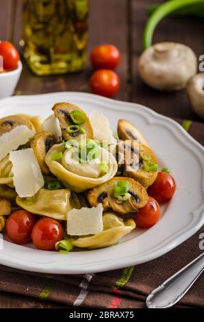 Des tortellini farci aux champignons et petits oignons, tomates confites, ail, parmesan surmontée source Banque D'Images