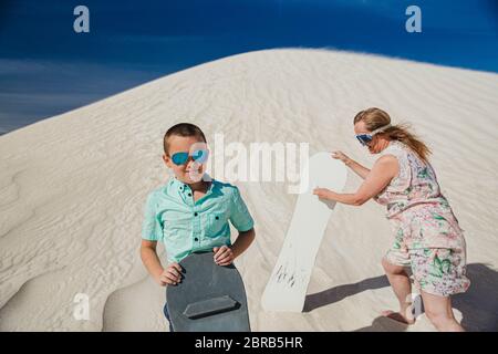 Portrait d'un petit garçon stadning sur une dune de sable à la Lancelin dunes de sable. Sa mère est debout derrière lui, jusqu'à la dune de sable avec un conseil de sable Banque D'Images