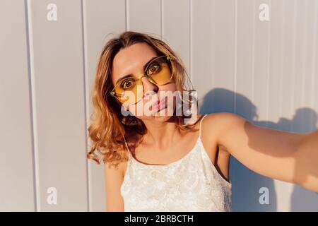 Crazy girl prend un attrayant, puffing out selfies ses joues, looking at camera, dans des lunettes de soleil. À l'extérieur. Banque D'Images