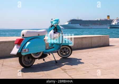 Le scooter bleu se dresse sur le front de mer, sur fond de bateaux de croisière par temps ensoleillé. Le scooter rétro bleu est stationné près de la mer avec un casque. De Banque D'Images