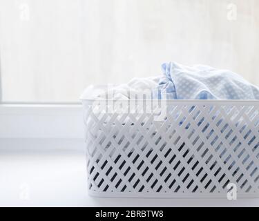 Des vêtements propres bleus et blancs dans un panier à linge en plastique sur un seuil de fenêtre sur un arrière-plan de fenêtre Banque D'Images