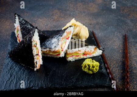 Délicieux sandwichs à sushis au saumon sur une assiette en pierre noire avec sauce soja, gingembre, wasabi Banque D'Images