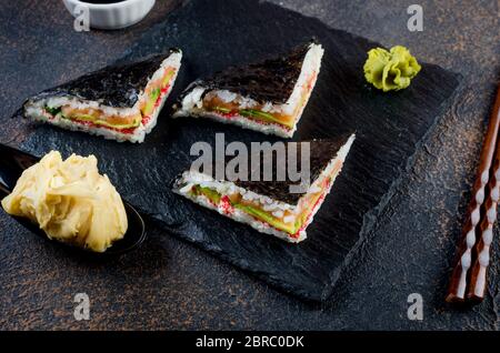 Délicieux sandwichs à sushis au saumon sur une assiette en pierre noire avec sauce soja, gingembre, wasabi Banque D'Images
