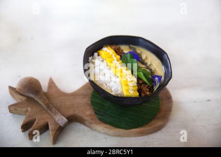 Bol à smoothie sain avec banane, granola et menthe sur un comptoir à ananas en bois. Manger propre. Banque D'Images