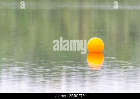 Vue sur un étang de carrière avec un accent particulier sur un marqueur de natation orange depuis la côte avec ciel couvert et eau calme dans le nord de l'Allemagne Banque D'Images