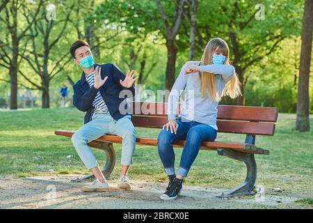 Homme et femme portant un masque sur un banc de parc dans un parc municipal, crise de Corona, Ratisbonne, Bavière, Allemagne Banque D'Images