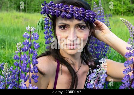 Une belle femme avec une couronne de fleur sur sa tête repose sur un champ de lupins en fleur lors d'une journée d'été ensoleillé Banque D'Images