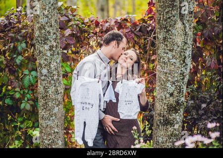 Une jeune femme enceinte et son mari. Une famille heureuse qui pendait des vêtements pour bébé sur une corde. Femme enceinte se détendant dans le parc. Banque D'Images