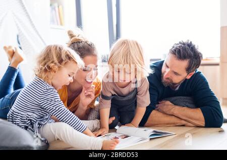 Une jeune famille avec deux petits enfants à l'intérieur dans la chambre à coucher lisant un livre. Banque D'Images