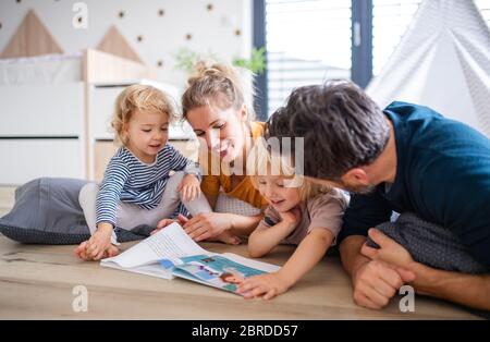 Une jeune famille avec deux petits enfants à l'intérieur dans la chambre à coucher lisant un livre. Banque D'Images