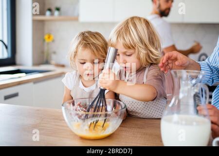 Jeune famille avec deux petits enfants à l'intérieur dans la cuisine, préparant la nourriture. Banque D'Images