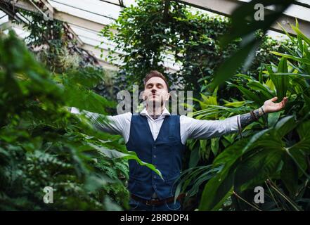 Jeune homme debout dans le jardin botanique, bras étirés. Banque D'Images