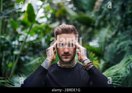 Homme fatigué dans la douleur debout dans le jardin botanique, concept d'affaires vertes. Banque D'Images