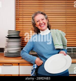 Femme laver à la main une grande pile d'assiettes, en regardant heureux Banque D'Images