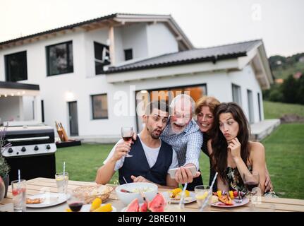 Portrait de personnes à l'extérieur sur le barbecue de jardin familial, en prenant le selfie. Banque D'Images