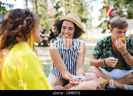 Groupe de jeunes amis au festival d'été, assis sur le terrain et manger. Banque D'Images