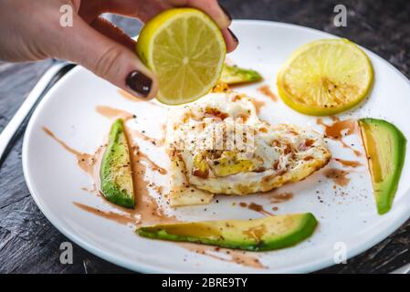 Un beau petit déjeuner romantique et sain d'œufs frits en forme de coeur avec des tranches d'avocat et de citron sur une assiette blanche. Banque D'Images