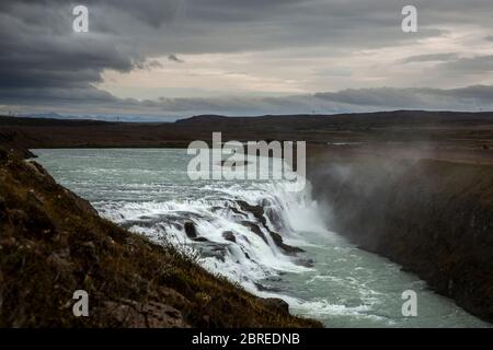 Vue générale de Gullfoss, l'une des plus grandes chutes d'eau du sud-ouest de l'Islande. Le ciel est bleu roi avec des nuages. Nous pouvons distinguer le ir du brouillard Banque D'Images