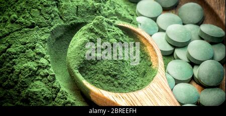 Algues vertes en poudre et pilules - chlorella, spiruline en bois cuillère sur fond de bois - gros plan - bannière design. Banque D'Images