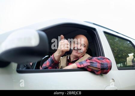 Homme hispanique senior conduisant une voiture et montrant le pouce vers le haut Banque D'Images
