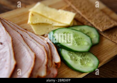 Trancher du jambon, des concombres et du fromage avec des pains fins et grossiers se trouvent sur une planche en bois. Banque D'Images