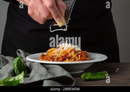 Pâtes bolognaises. Râper le fromage à la main sur des spaghetti Banque D'Images